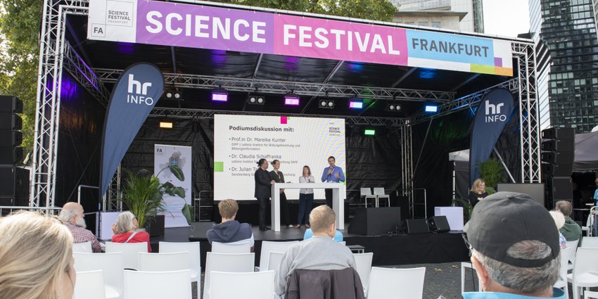 Audience watching a panel discussion on the main stage at the Frankfurt Science Festival, with speakers standing in front of a large presentation screen.